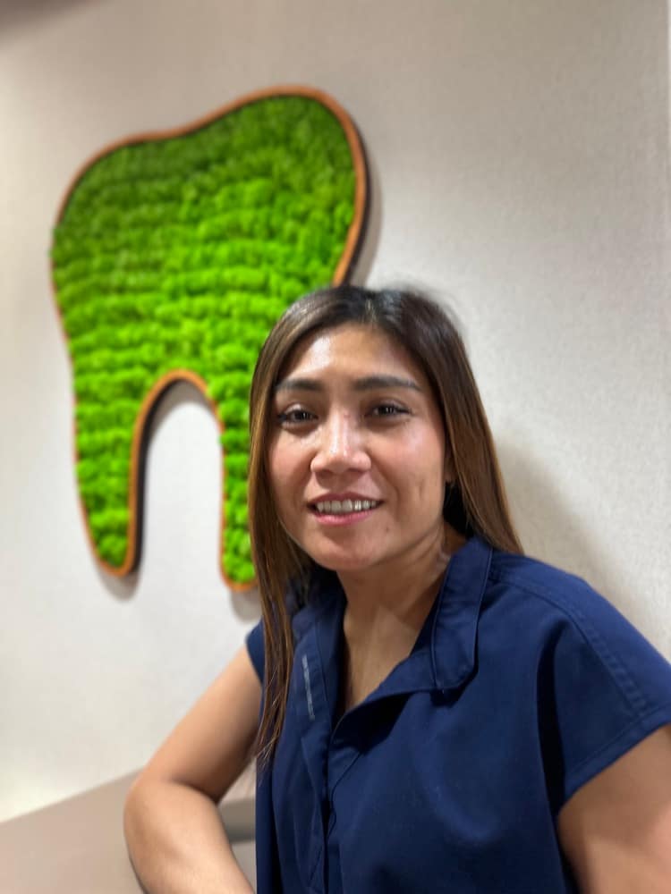 Family First Smile Care dental assistant beside the office moss-tooth wall